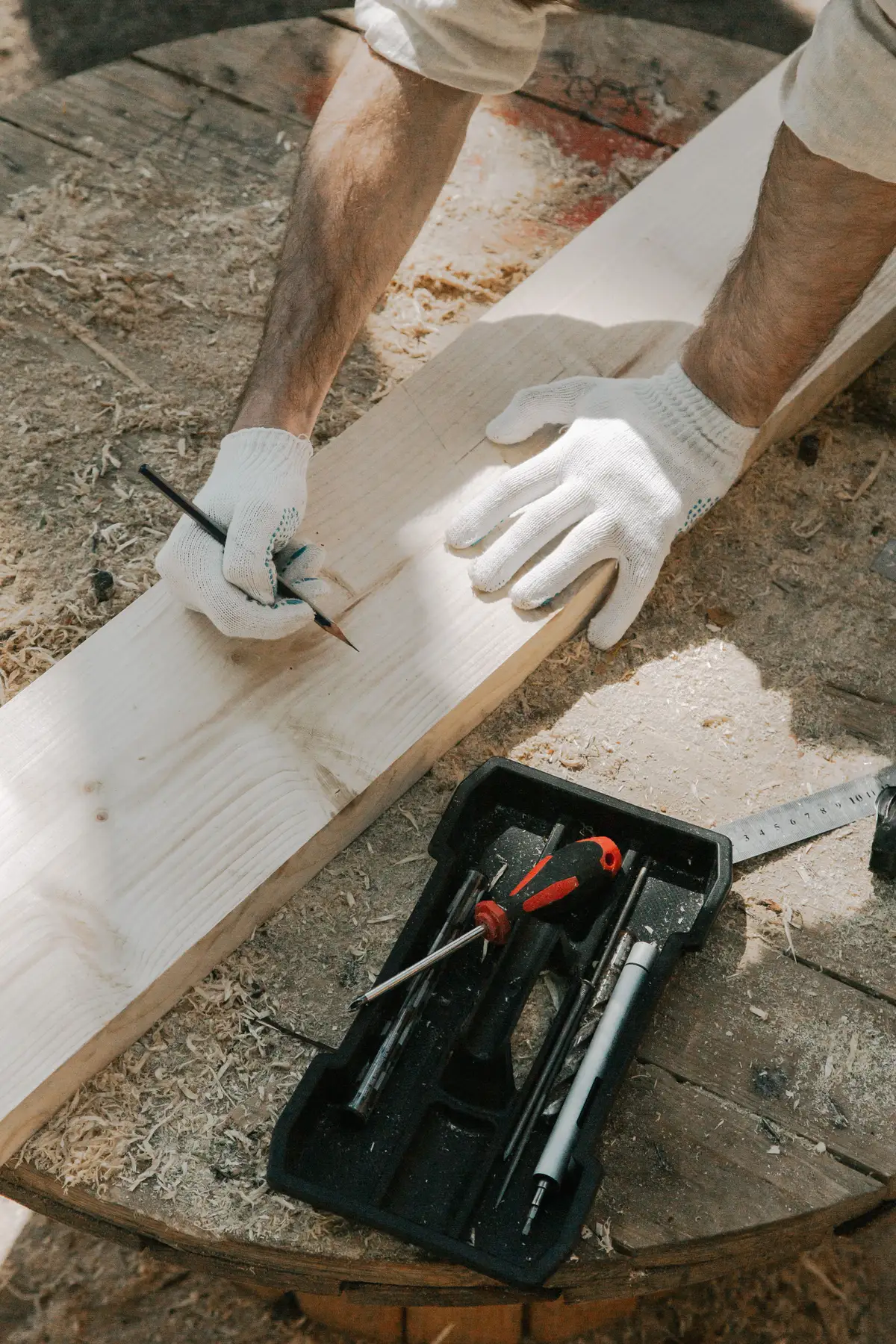 Traçage au crayon sur une planche de bois, gants et outils à proximité